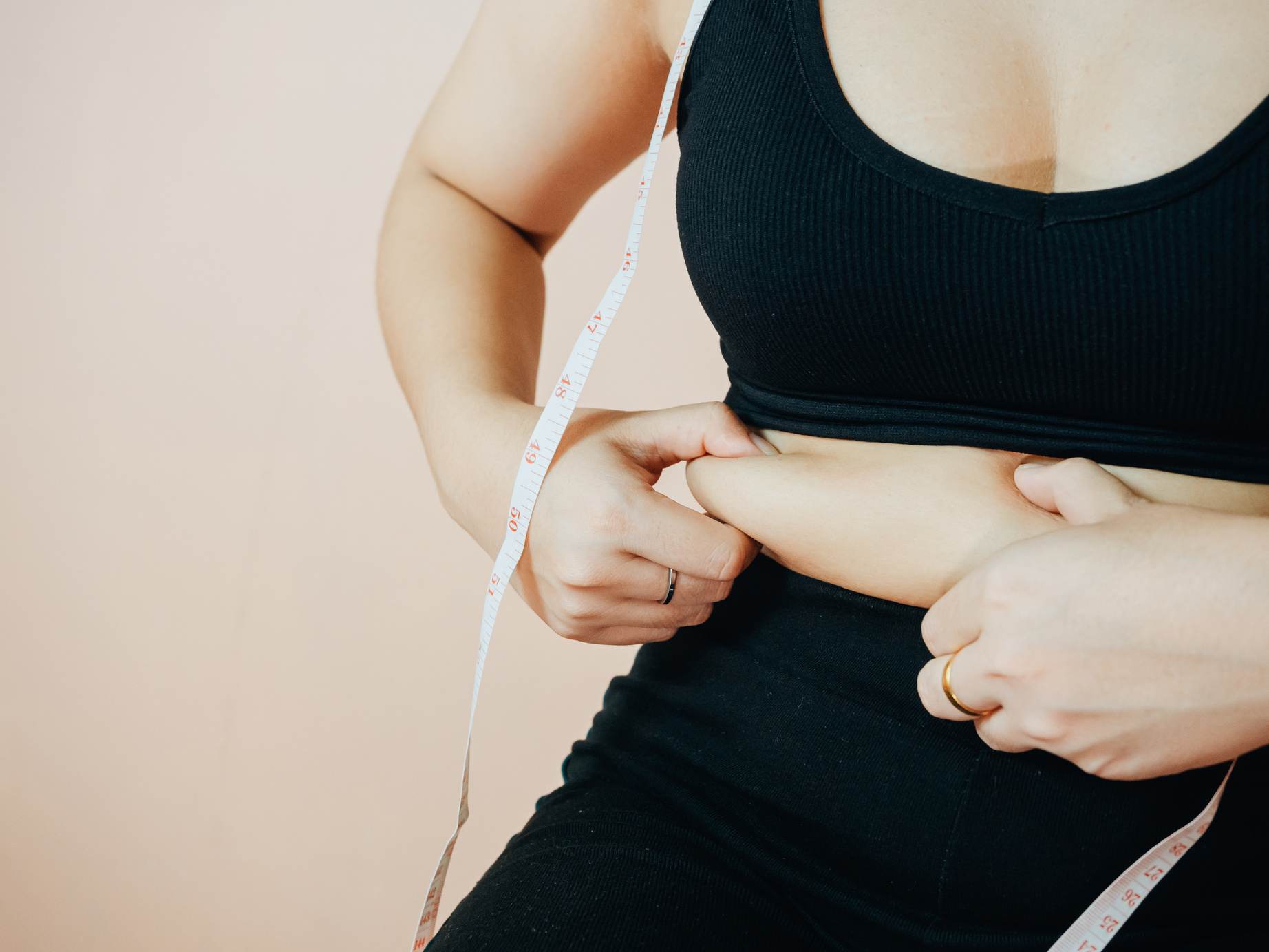 Lose belly fat concept from close up woman in sportswear with hand holding her own belly fat and cellulite.